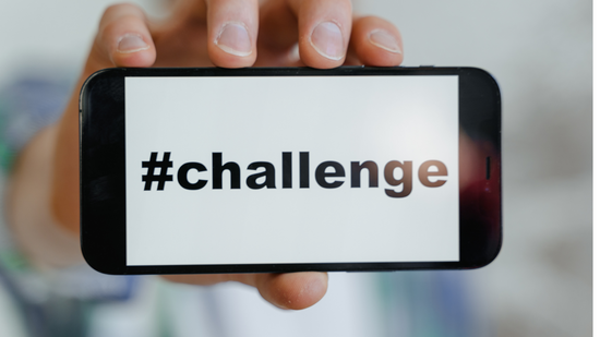 Ein junger Mensch, der Handy mit #Challenge Schriftzug in der Hand h&auml;lt 